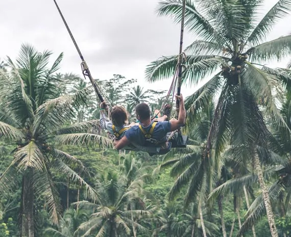 Couple sur une balançoire au milieu d'une foret de palmiers
