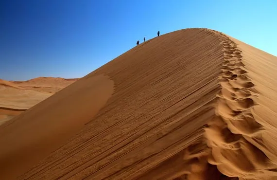 Personnes se tenant au sommet d'une dune sur fond de ciel bleu