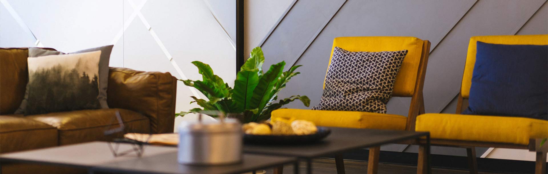 intérieur cosy d'une salle d'attente avec un canapé marron, des fauteuils jaune moutarde avec des coussins, une table basse et une plante verte