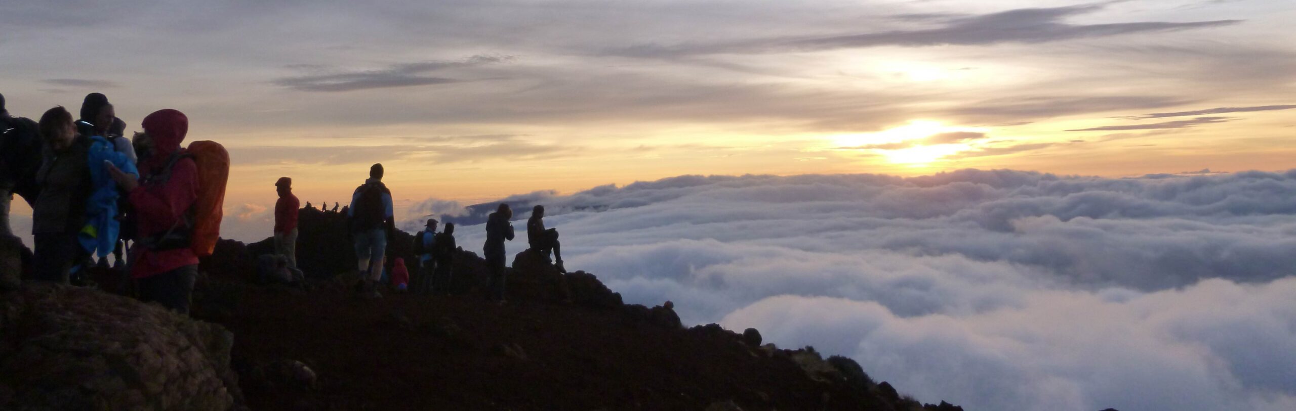 groupe de randonneurs au sommet d'une montagne, au dessus d'une mer de nuage, au lever du soleil