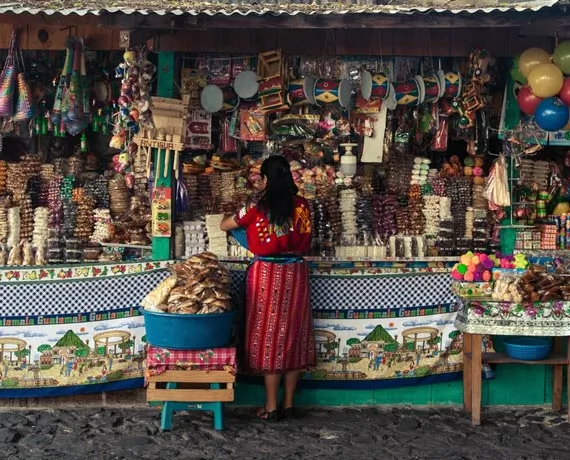 Femme vetue de rouge se tenant devant un stand de souvenirs dans un marché en Equateur