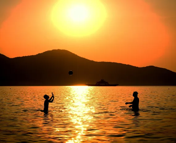 Famille jouant au ballon dans l'eau sur fond de coucher de soleil