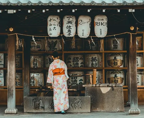 Femme en kimono blanc et orange devant un temple japonais