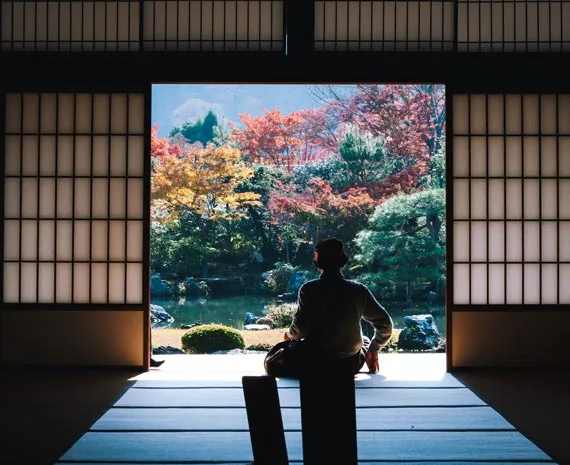 Personne se tenant dans l'encadrure d'une porte typique et contemplant un jardin japonais