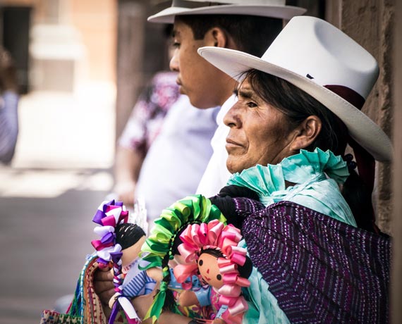 Femme coiffée d'un chapeau et vetue de manière traditionnelle portant des poupées