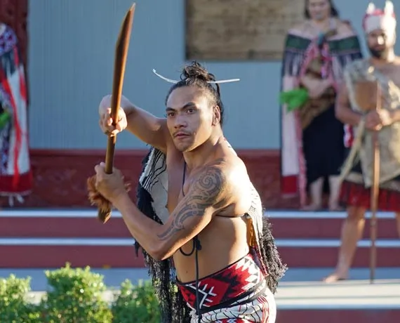 Guerrier maori tenant un baton en bois et vetu de manière traditionelle en Nouvelle-Zélande