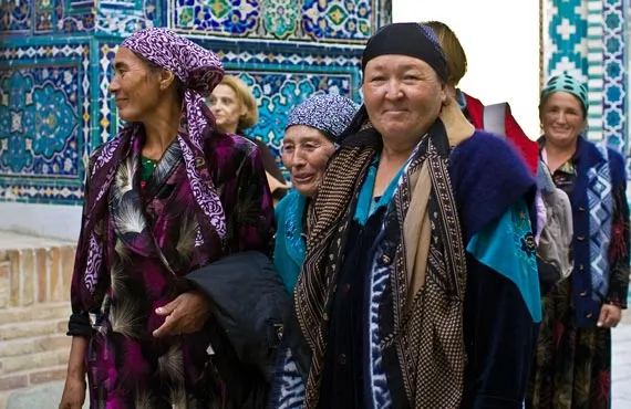 Femmes ouzbeques vetues de manière traditionnelle marchant devant un mur couvert de mosaiques bleues