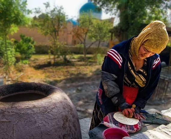 Femme vetue d'un costume traditionnel en train de cuisiner un pain ouzbek