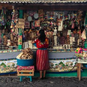 Femme vetue de rouge se tenant devant un stand de souvenirs dans un marché en Equateur