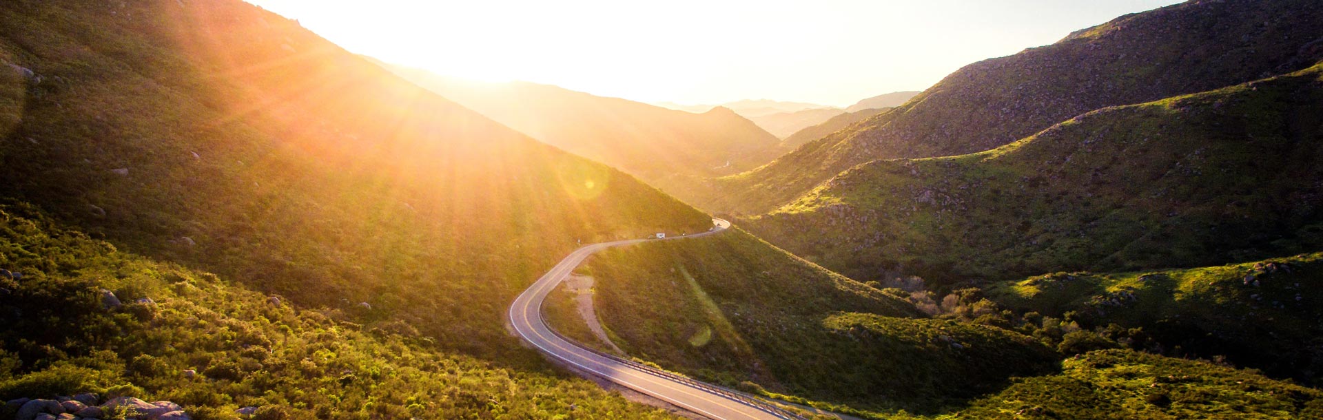 route qui serpente dans un paysage de collines recouvertes de végétation, au coucher du soleil