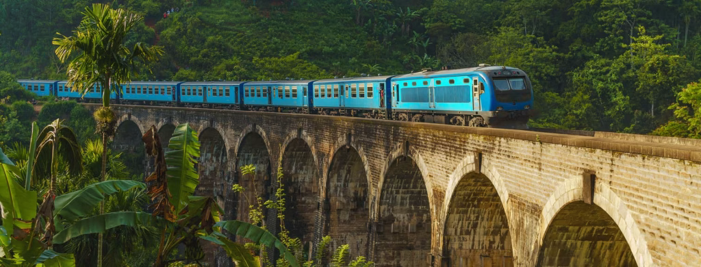 Train aux wagons bleus sur un pont traversant la végétation luxuriante, au Sri Lanka