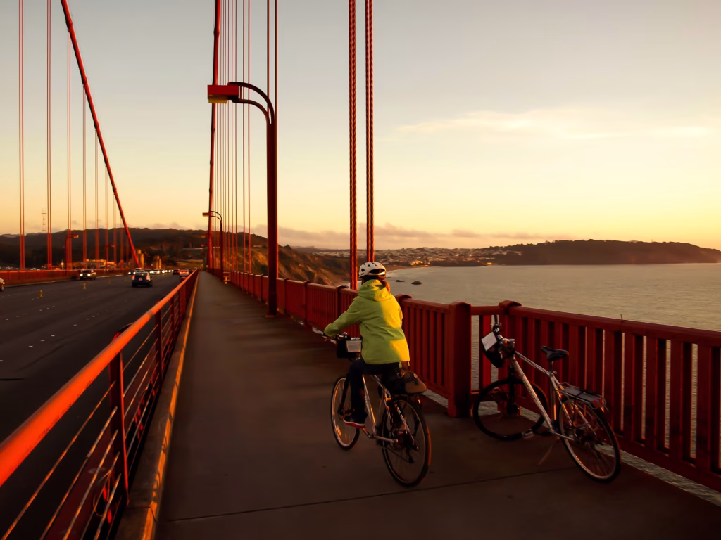 Une dame à vélo traversant le Golden Gate Bridge au coucher du soleil, San Francisco, Amérique de l'ouest