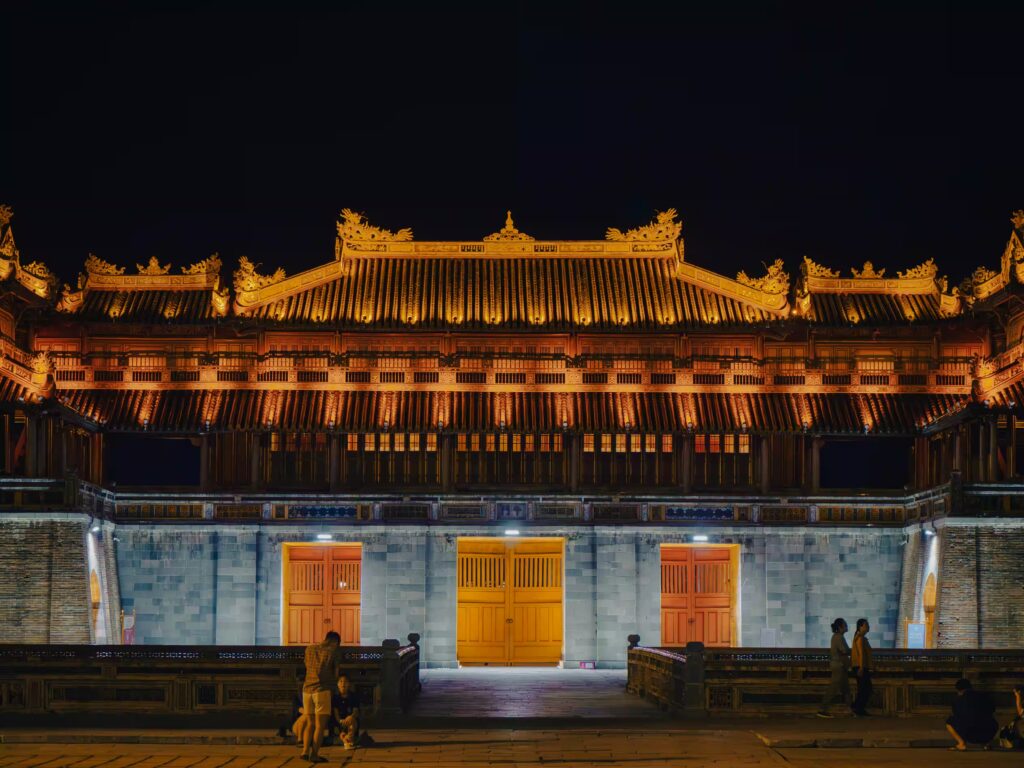 Temple illuminé sur le toit et porte la nuit avec passants, Vietnam