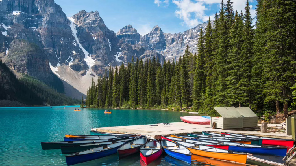 Lac aux eaux turquoie au pied de montagne, canoés colorés au premier plan, rives bordées de grands sapins - Lac Moraine, Parc national Banff, Alberta, Canada