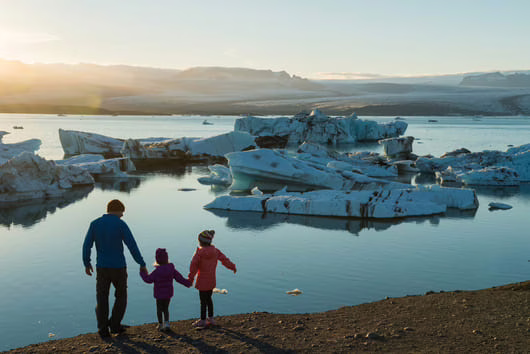 Famille avec enfants sur une plage de sable noir, face aux morceaux d'icebergs dans la lagune glaciaire Jokulsarlon, Islande