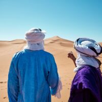 Deux personnes portant un linge blanc sur enroulé et attaché la tête devant une dune de sable