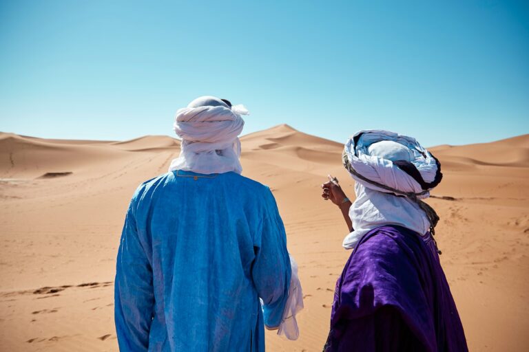 Deux personnes portant un linge blanc sur enroulé et attaché la tête devant une dune de sable