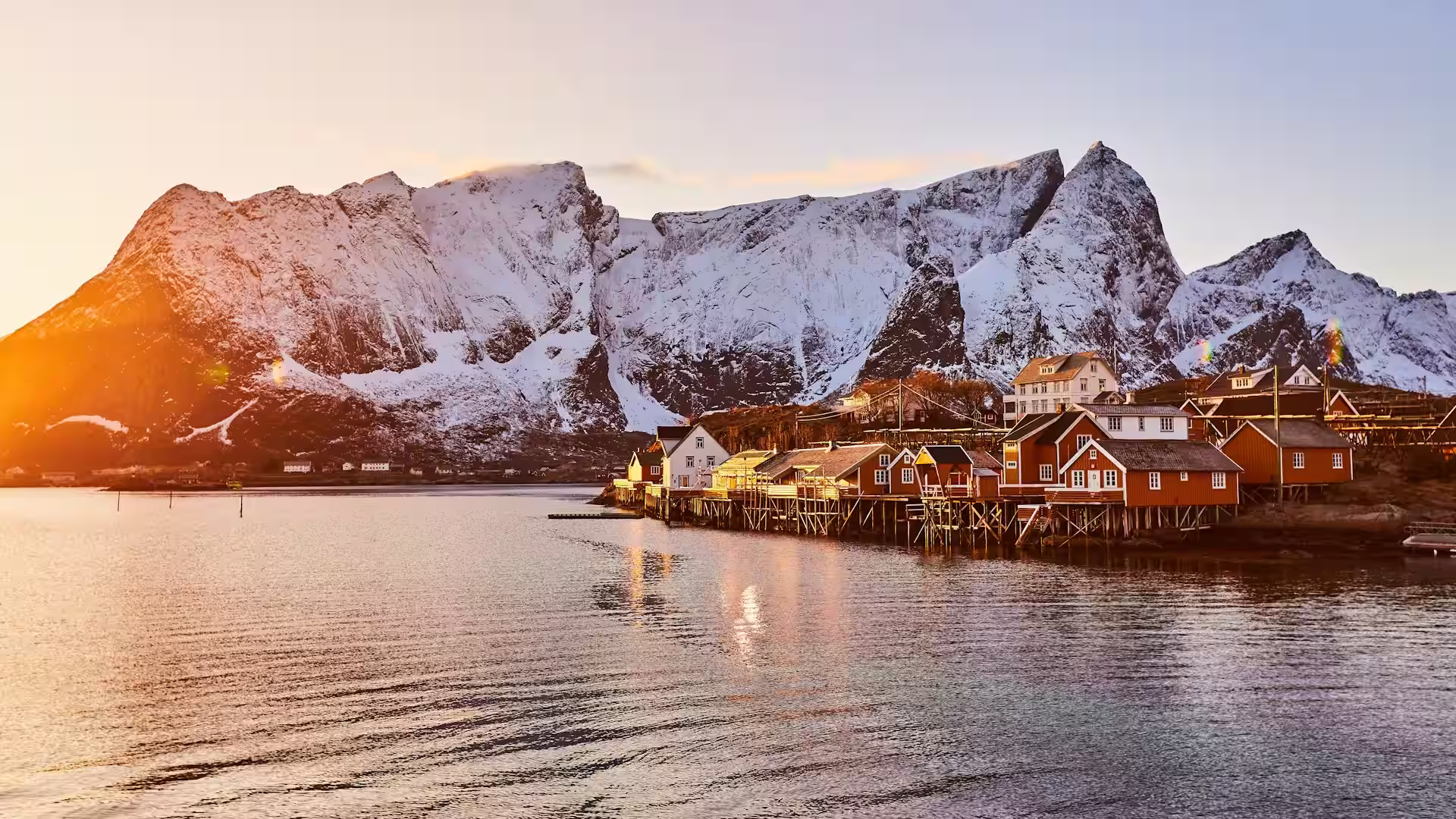 Coucher de soleil sur montagnes enneigées et maisons rouges sur pilotis