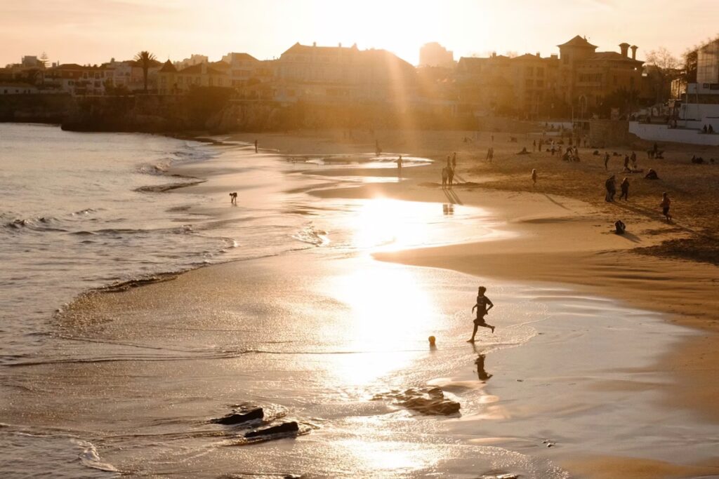 PLage au coucher du soleil descendant derriere les batiments et maisons au loin, personnes jouant au ballon