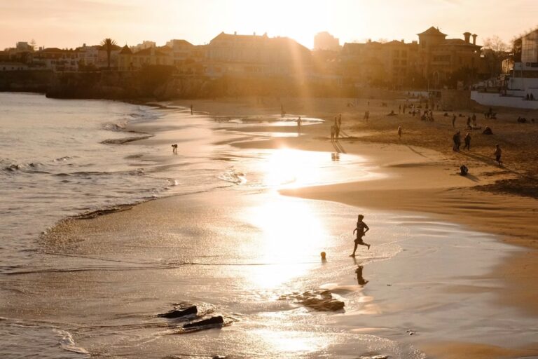 PLage au coucher du soleil descendant derriere les batiments et maisons au loin, personnes jouant au ballon