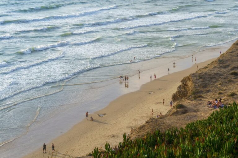 Plage de sable blanc avec petite falaise et végtation, personnes mrchant le long de la plage