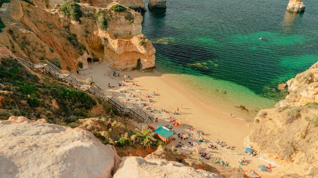 Vue du haut d'une falaise, la plage en contrebas avec escalier permettant d'y descendre, des personnes sont allongés sur serviettes et certains sous parasols