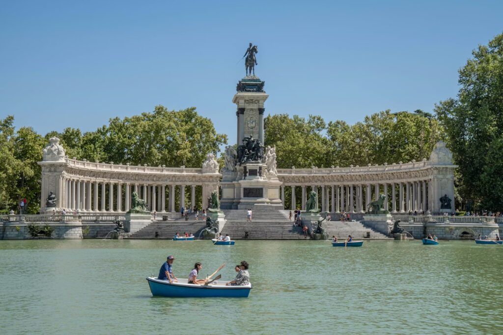 Bassin deau avec barques, monument en arc de cercle avec des colonnes et statues et végétation en arriere plan