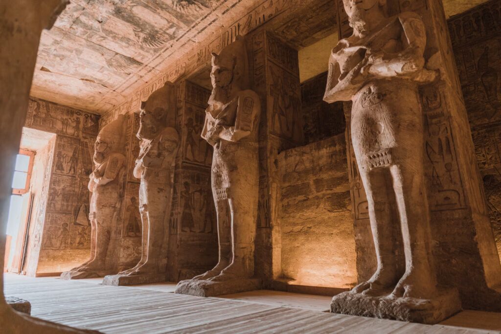 Porte entrée dans une pièce à l'éclairage tamisé et très grandes statues alignées et murs reciuverts de dessins et hiéroglyphes