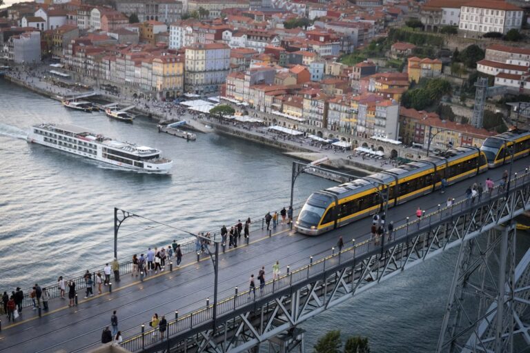 Tram traversant un pont avec passants, fleuve avec bateau de croisiere fluviale, rive du fleuve avec habitations, commerces et passants