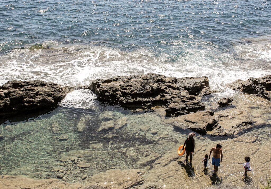 Vue d'une hauteur, la mer et ses vagues sur la roche formant une petite piscine naturelle et une famille
