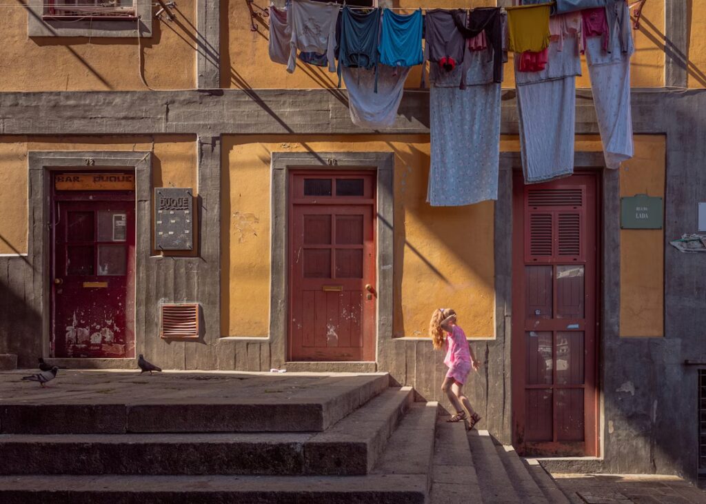 Petite fille montant escalier dans la rue devant une façade d'immeuble jaune te groses avec porte couleurs terra cotta
