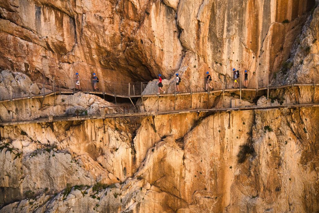 Pan de montagne avec un chemin en bois qui longe la falaise et des personnes