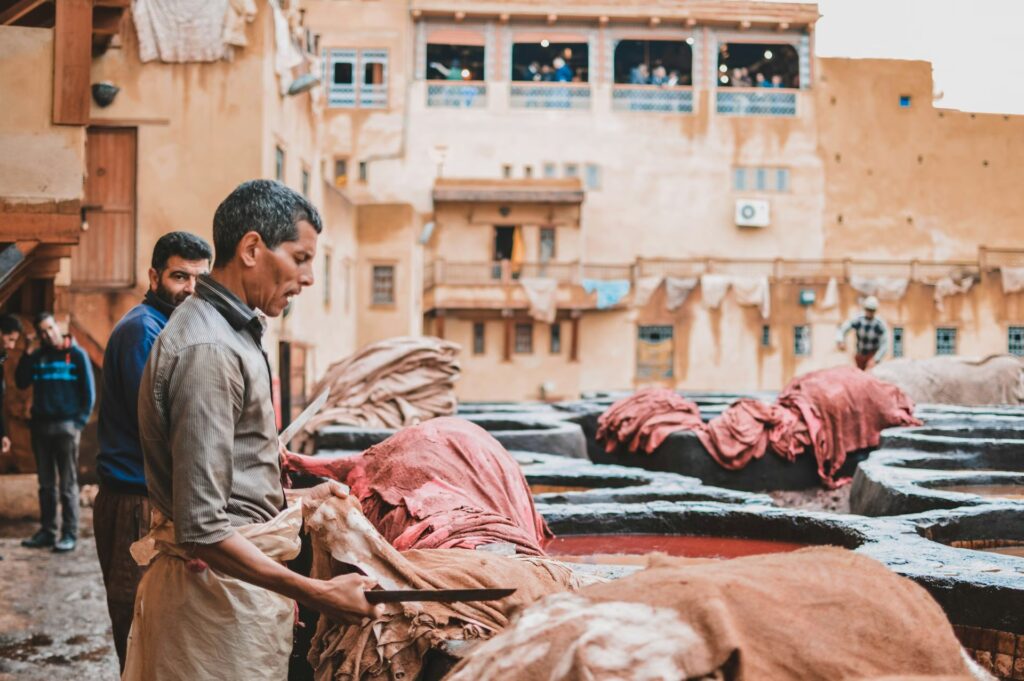 Hommes tenant du linge dans ses mains avec uen planche, au bord des bassins remplis d'eau colorée