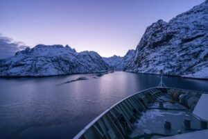 Montagnes enneigées avec lumiere du soir et proue d'un bateau sur l'eau