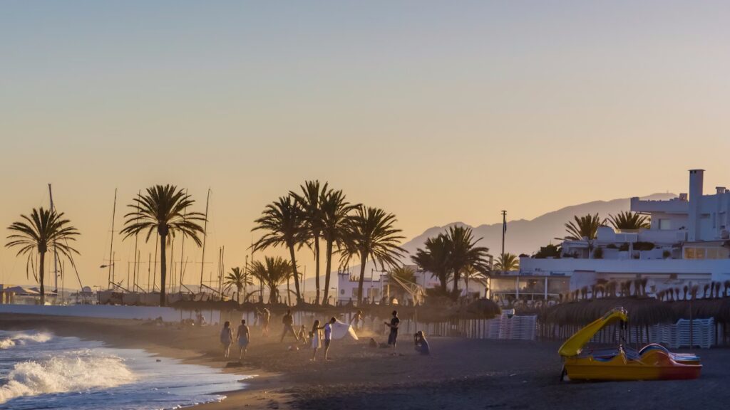 PLage de sable blanc avec vagues, palmiers, personnes, batiments blancs