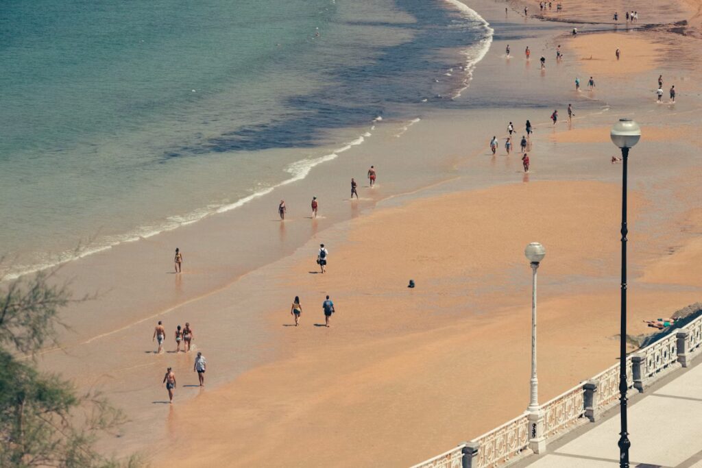 Large plage de sable blanc, personnes marchand le long de la mer, corniche avec lampadaires