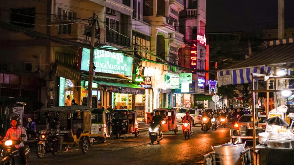 Rue commerçante de nuit avec scooters, tuk-tuk et voitures