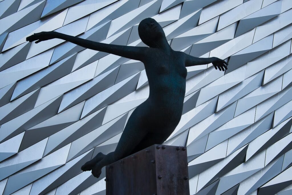 Statue sur un pied d'estale en positien de voler, en arriere pla, un mur moderne fait de rectangle plus ou moins bien encastrés