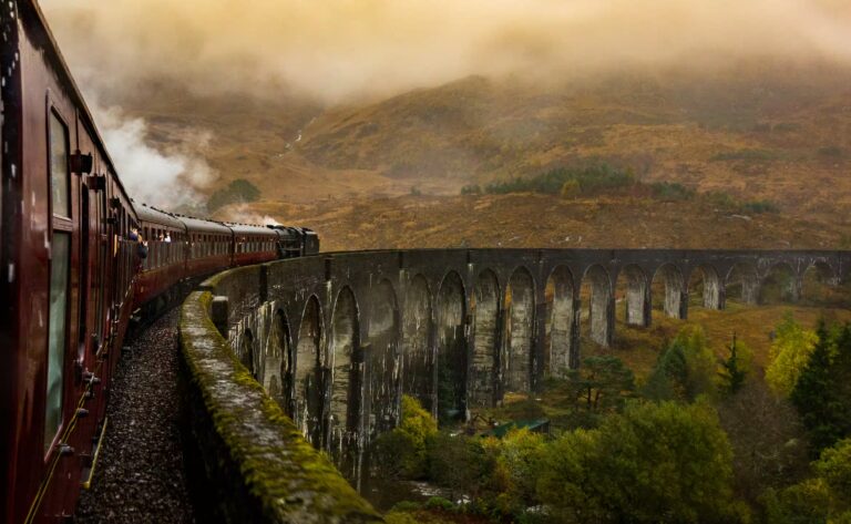 Viaduc avec train rouge et collines recouverte de vegetation jaune et nuage