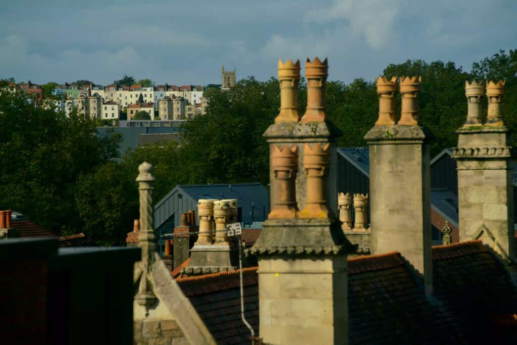 Vue sur les cheminés des toits d'habitation et des immeubles en fond avec de la végétation au milieu