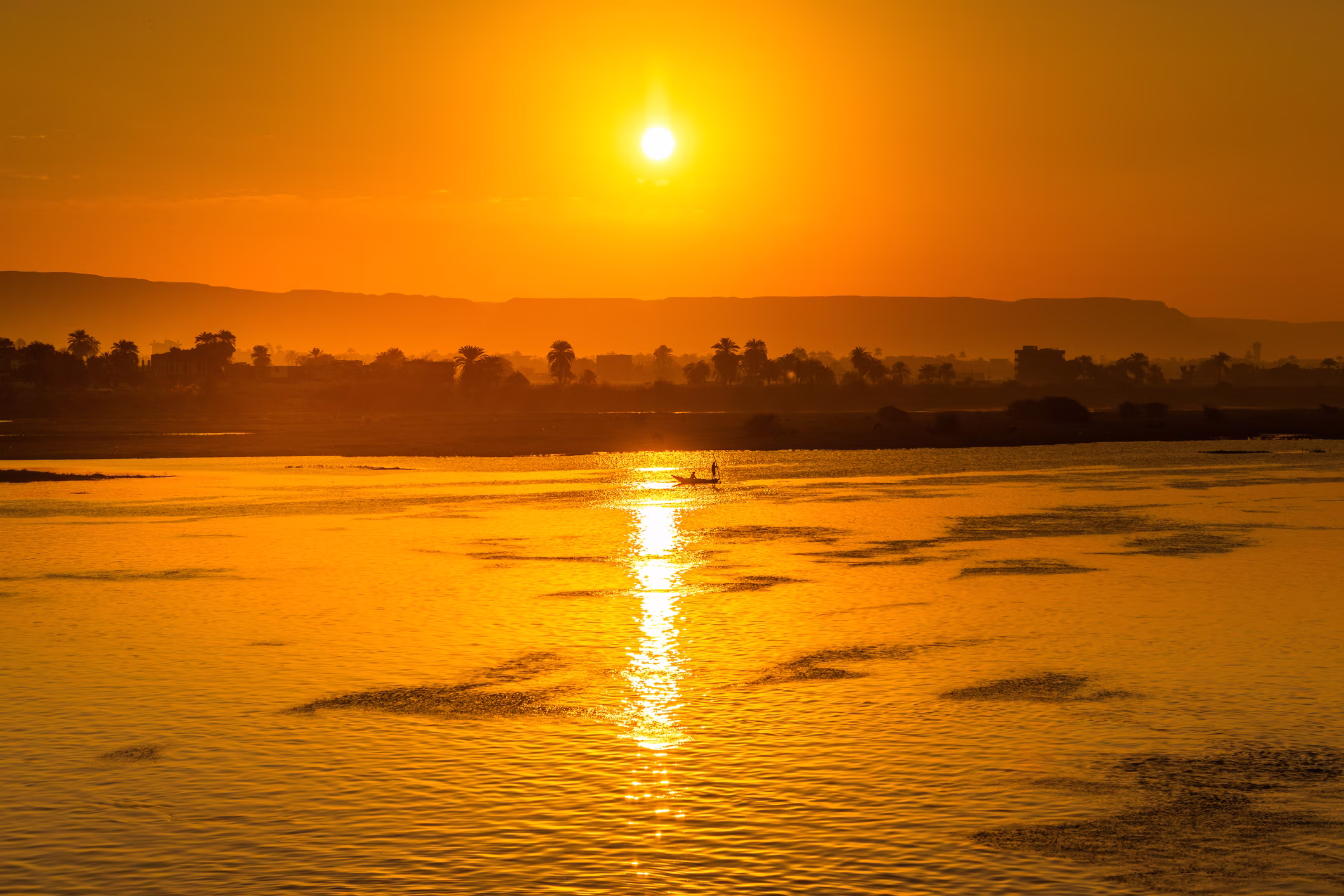 Coucher de soleil de puis une rive d'un fleuve avec palmiers en ombre et un bateau avec deux personnes