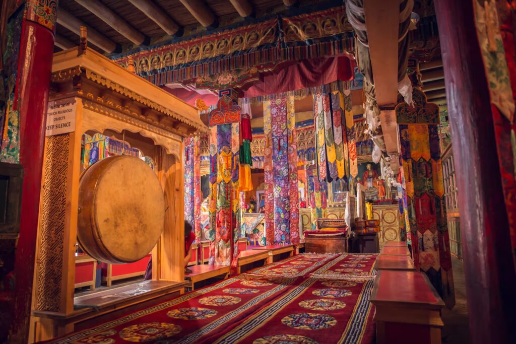 Interieur d'un temple rempli de tissus colorés et à motifs, accroché au planfond, tapis par terre, banc et un gong