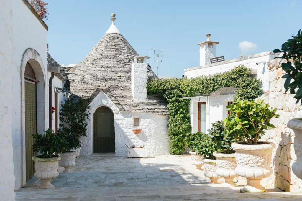 Maison au toit pointu et de pierres avec murs blancs, pots de plantes vertes