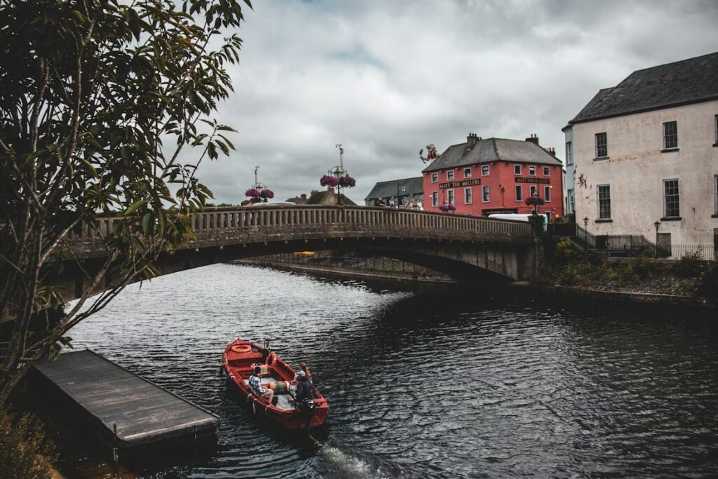 Petit bateau rouge sur le fleuve surmonté d'un pont en pierre avec sur la rives des batiments