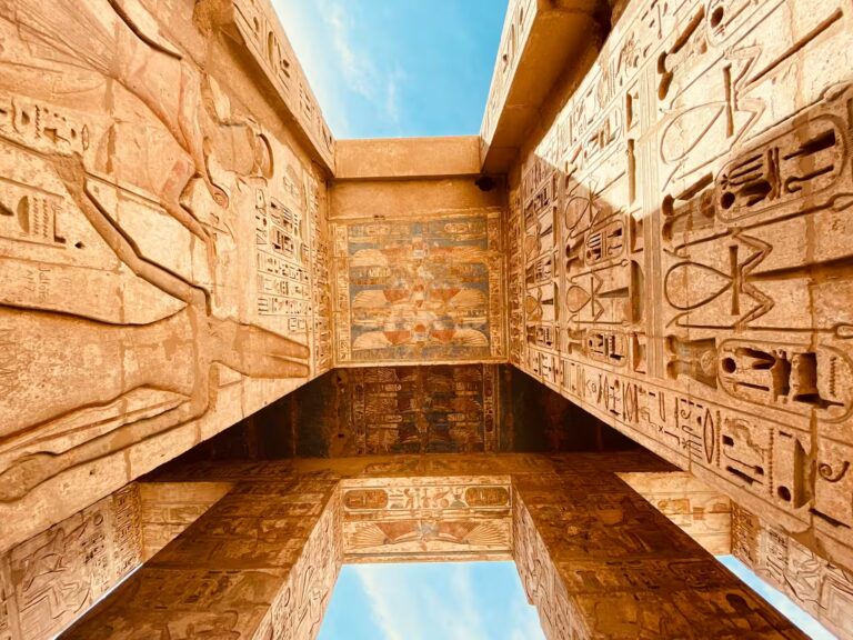 Mur et plafond recouvert de gravures, hieroglyphes et peintures avec une ouverture vers le ciel bleu
