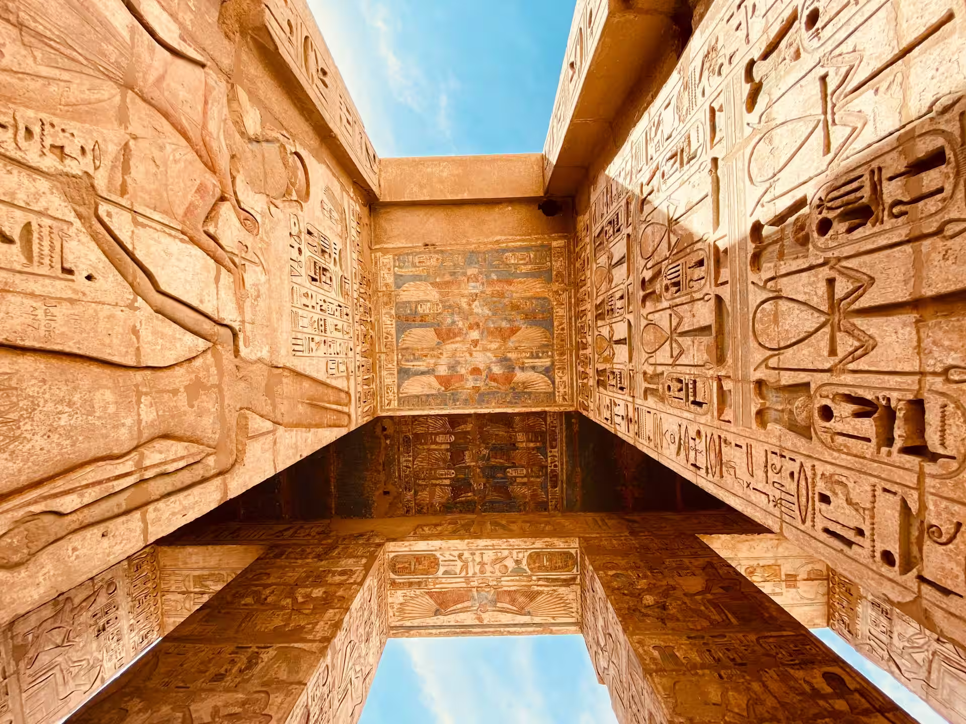 Mur et plafond recouvert de gravures, hieroglyphes et peintures avec une ouverture vers le ciel bleu