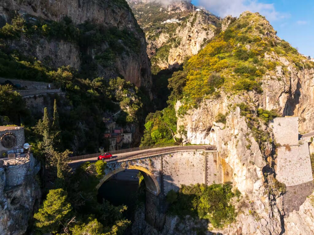 Falaise avec végétation, pont traversé par une voiture rouge