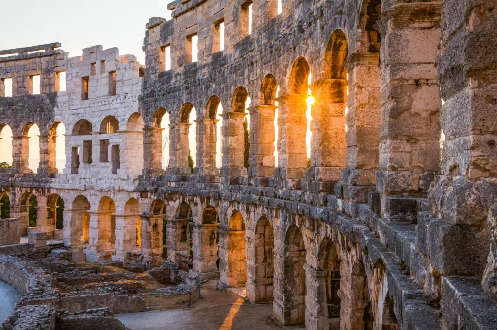 Monument en pierre, en ruines avec arcades ou la lumiere du soleil couchant passe