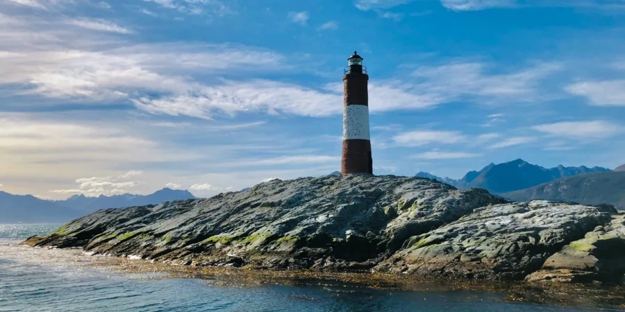 phare brun et noir sur une colline rocheuse pres dun plan deau sous des nuages bleus et blancs hNdDLuLgz